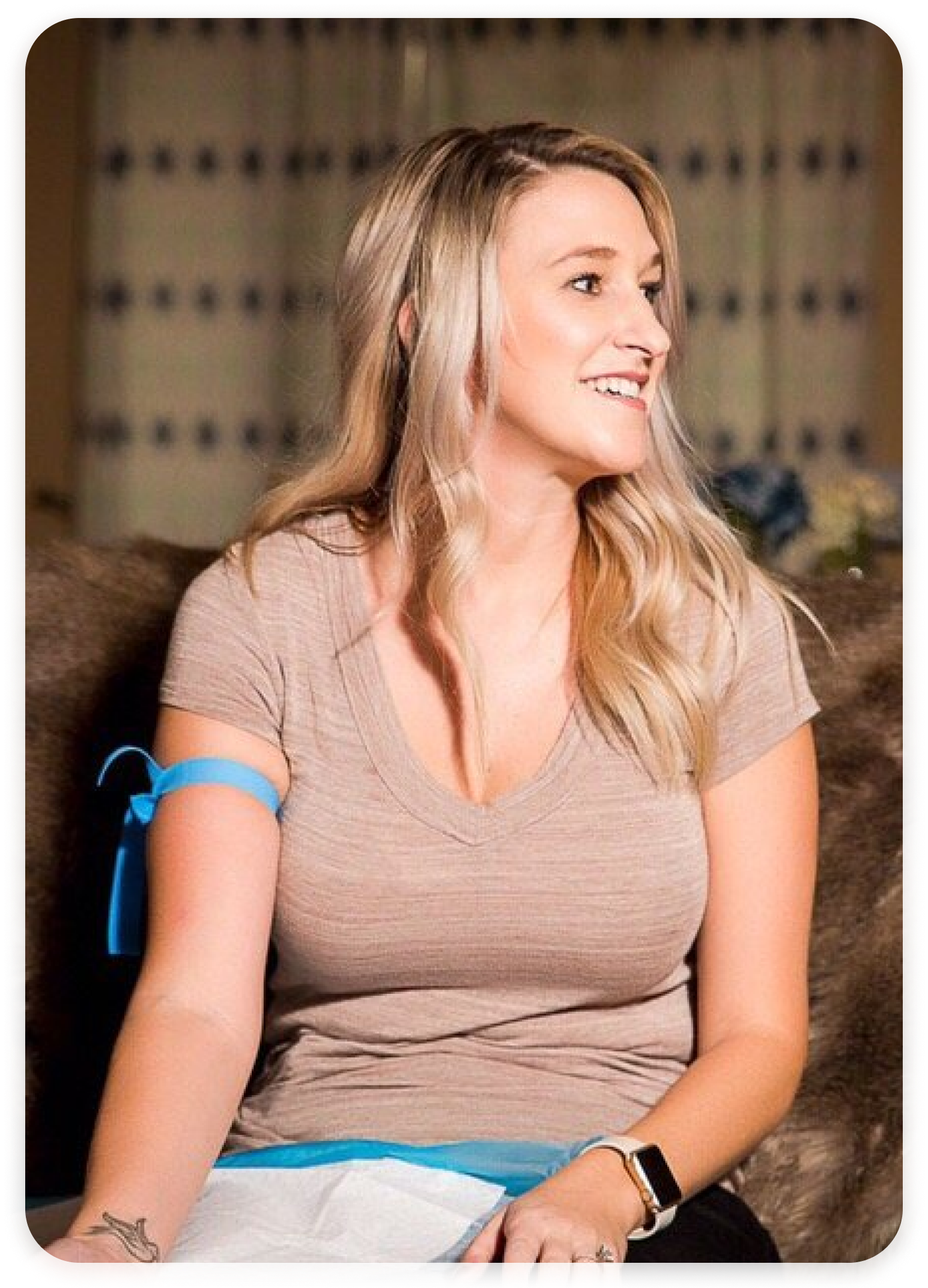 A woman is sitting on a couch with a blue bandage on her arm.