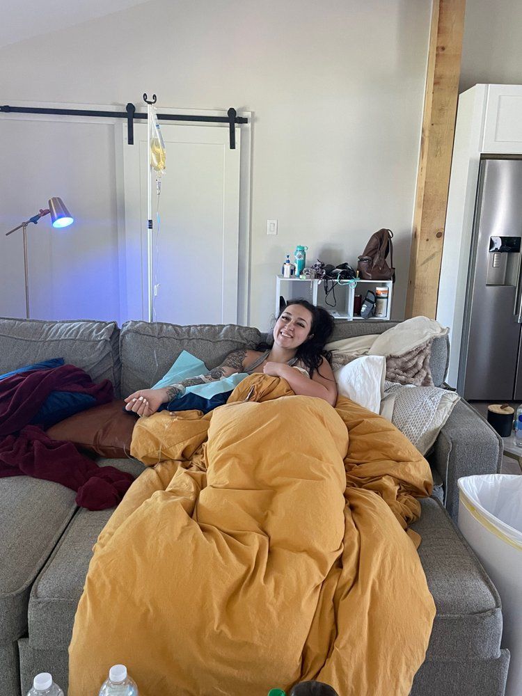 A woman is laying on a couch wrapped in a yellow blanket.