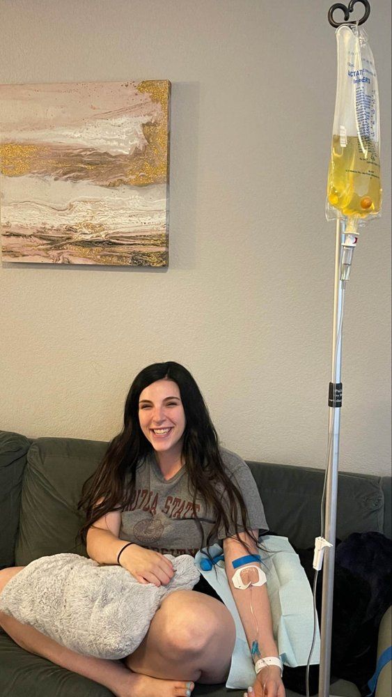A woman is sitting on a couch with an iv in her arm.