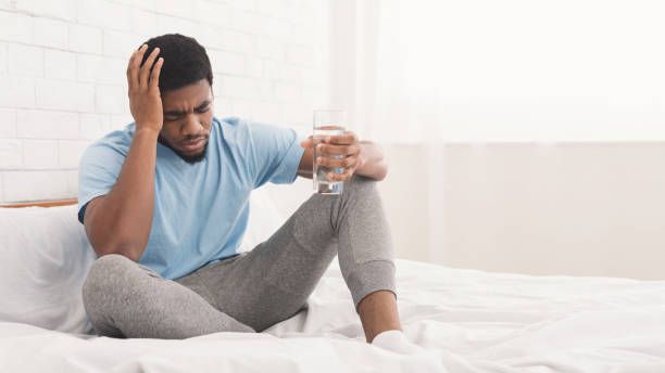 A man is sitting on a bed holding a glass of water.
