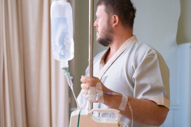 A man is standing in a hospital room with an iv in his hand.