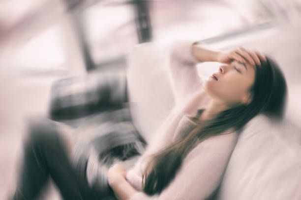 A woman is sitting on a couch with her hand on her forehead.