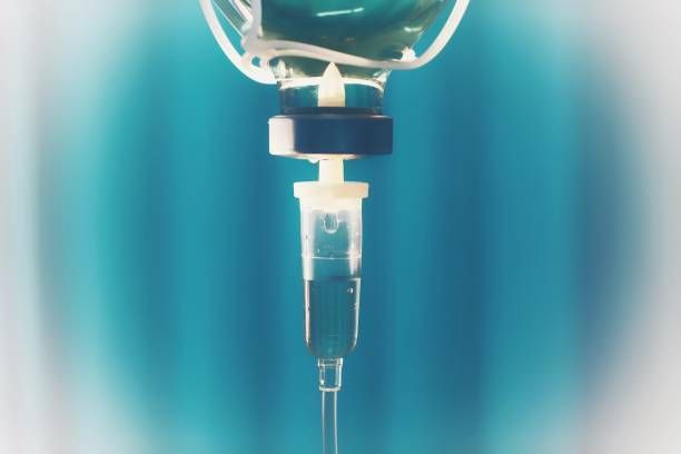 A close up of an intravenous drip with a bottle of liquid hanging from it.