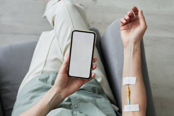 A woman is sitting on a couch with an iv in her arm and holding a cell phone.