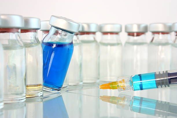 A syringe is sitting next to a row of bottles of vaccine.