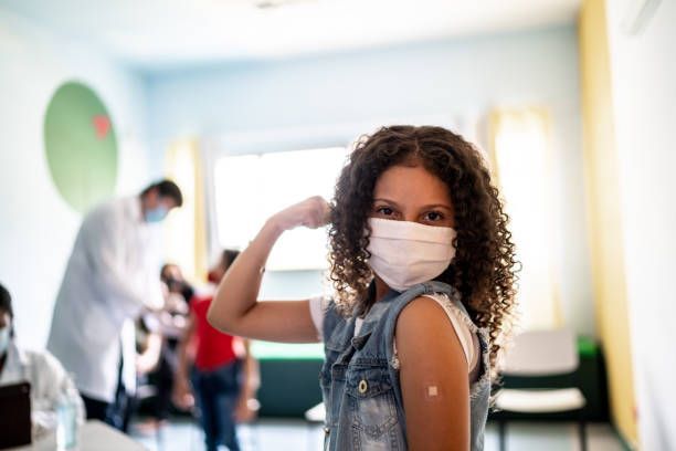 A young girl wearing a mask is giving a fist bump after getting a vaccine.