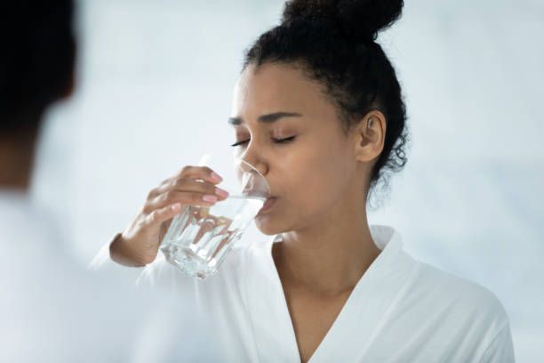 A woman is drinking a glass of water in front of a mirror.