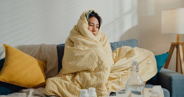 A woman wrapped in a blanket is sitting on a couch.