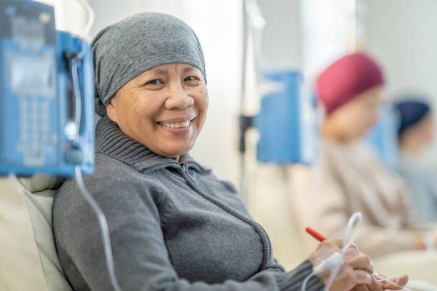 A woman with cancer is smiling while sitting in a hospital bed.