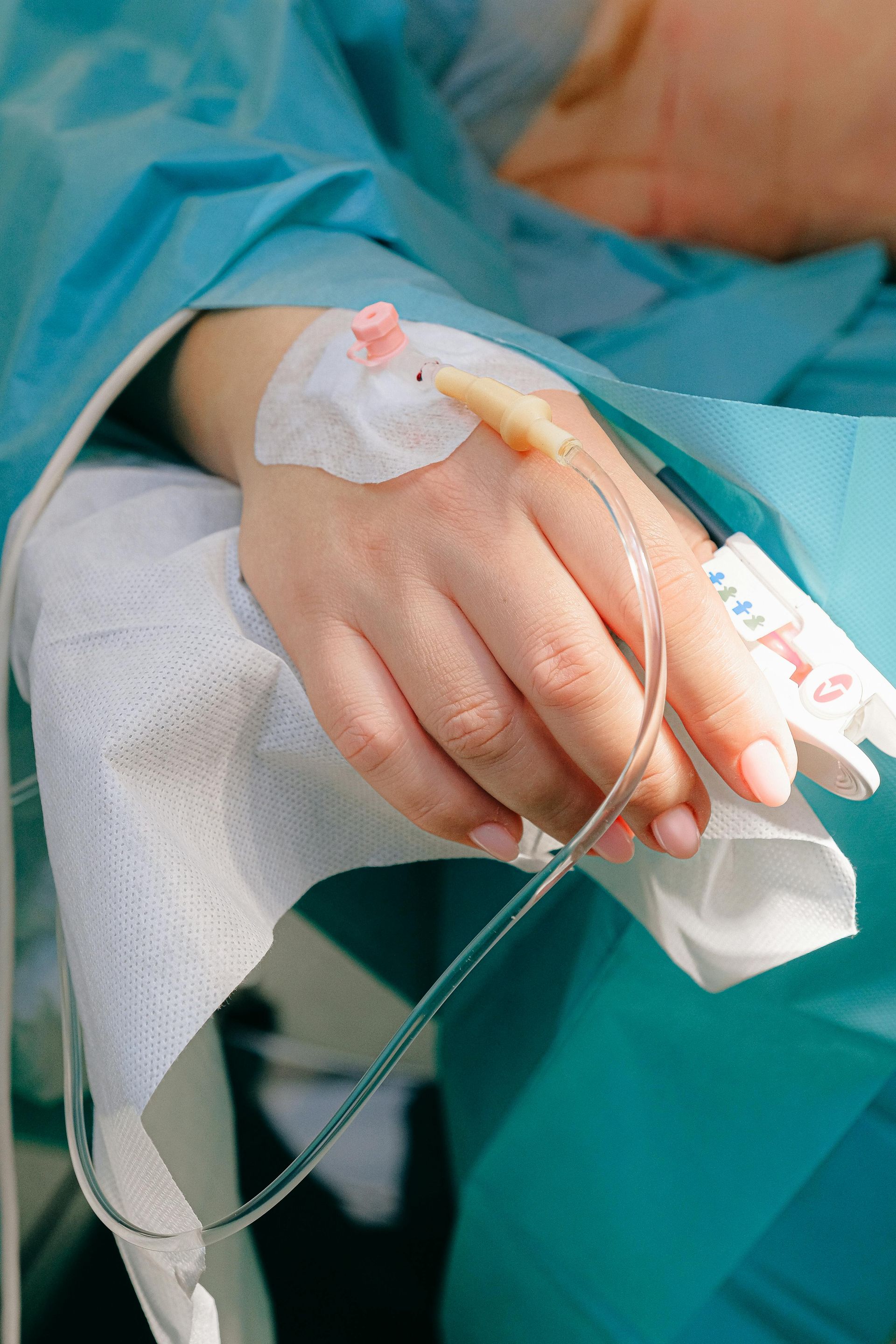 Hand with IV line inserted, on a surgical drape; person in medical setting.