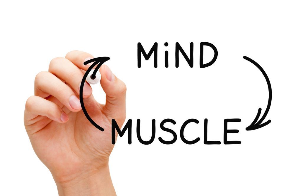 A hand is writing the word mind muscle with a marker.