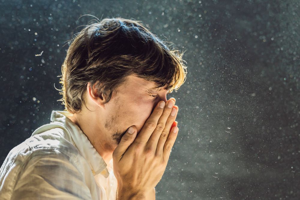 A man is covering his face with his hands while sneezing.