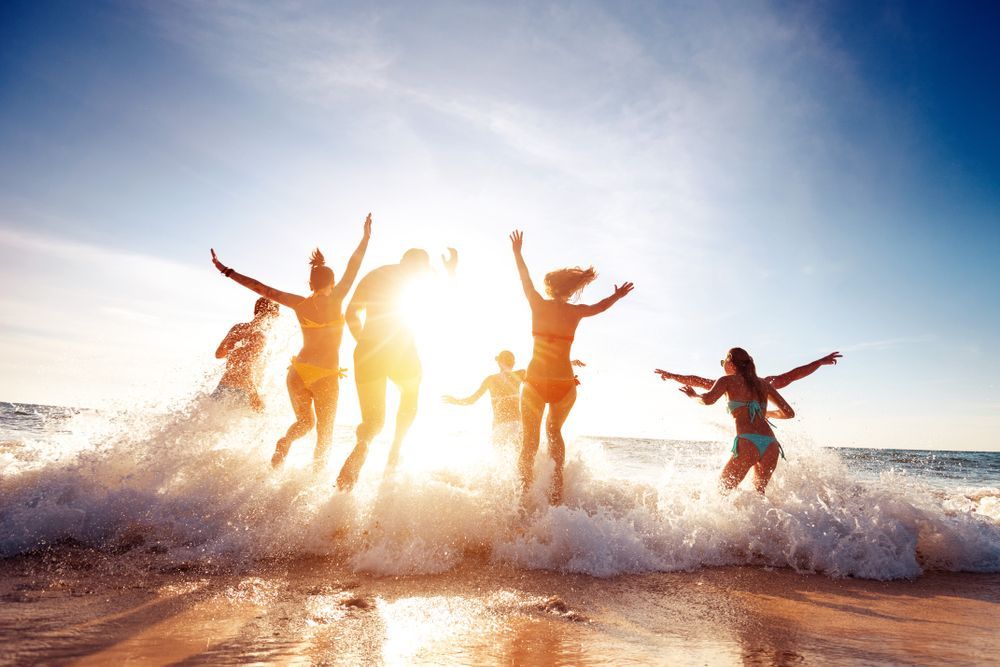 A group of people are jumping into the ocean on a beach.