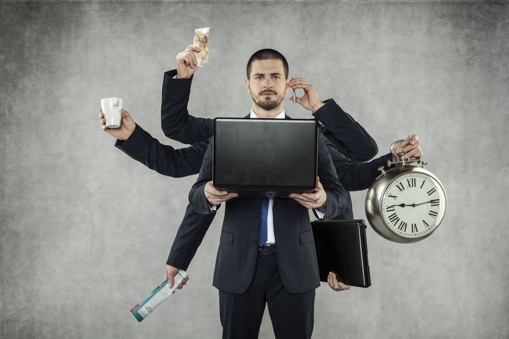 A man in a suit has many hands holding a laptop and a clock.