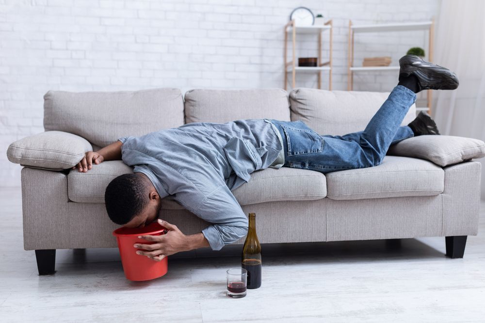 A man is laying on a couch with a bucket in his mouth.