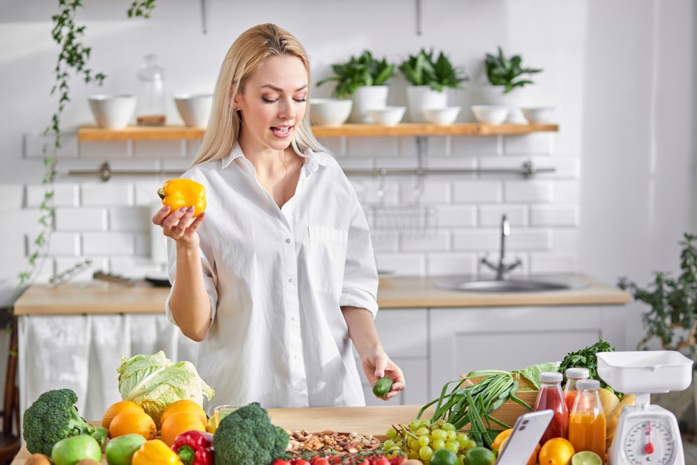 A woman is standing in a kitchen holding a yellow pepper.