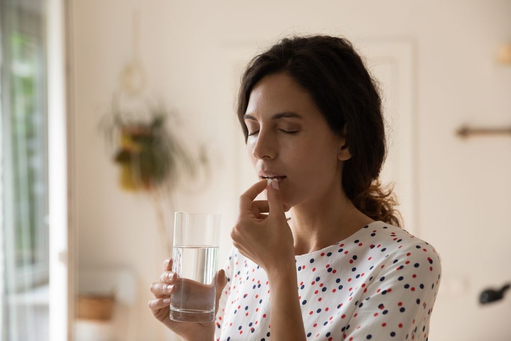 A woman is taking a pill and drinking a glass of water.