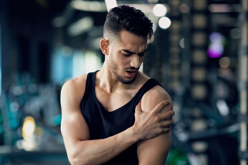 A man is holding his shoulder in pain in a gym.