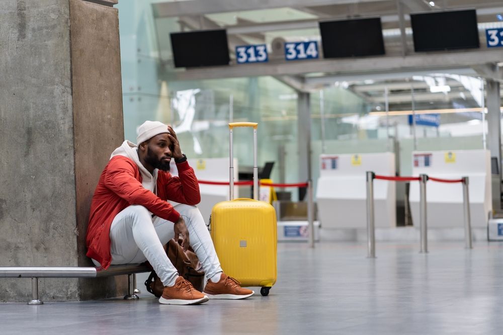 A man is sitting on a bench at an airport with his luggage.