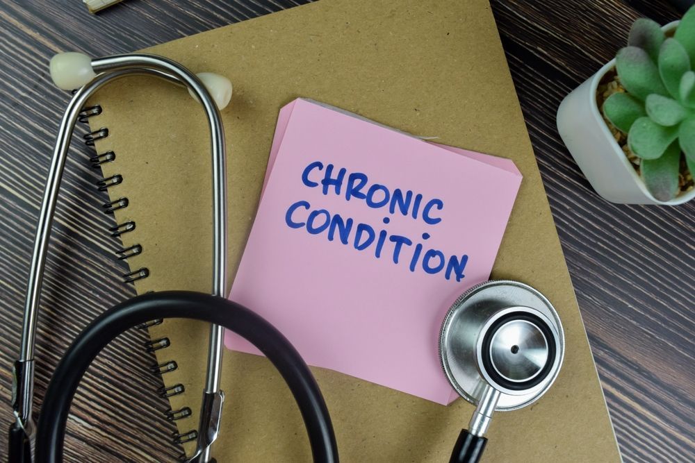 A stethoscope is sitting next to a pink sticky note that says chronic condition.