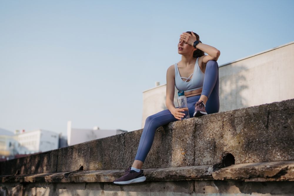 A woman is sitting on a wall with a bottle of water.