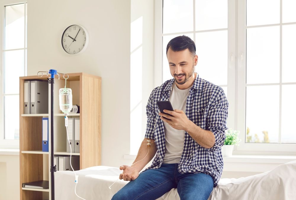 A man is sitting on a bed looking at his cell phone.