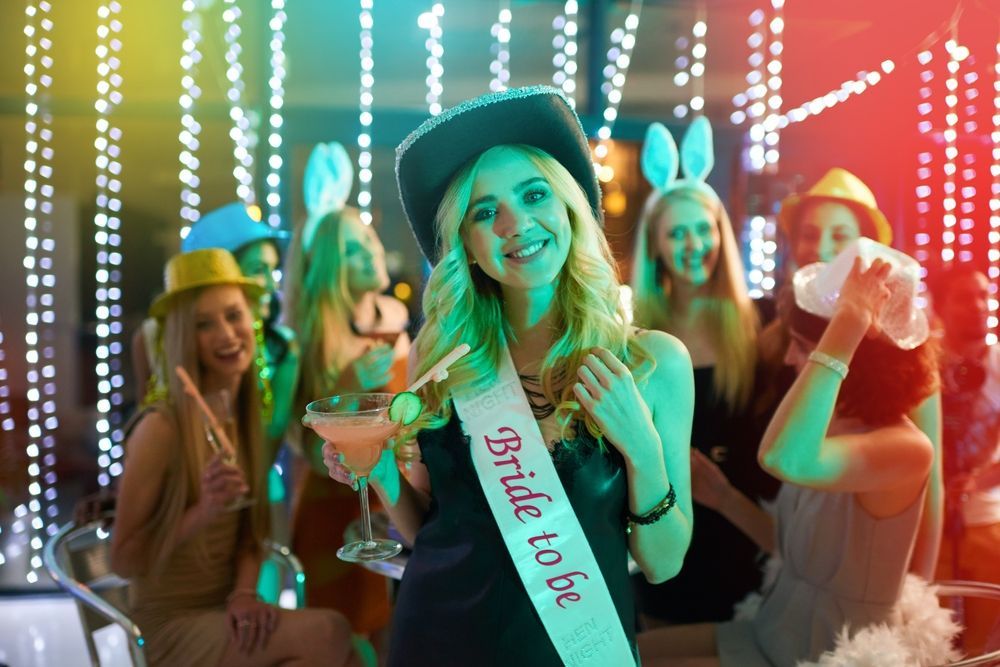 A woman is wearing a sash that says `` bride to be '' at a bachelorette party.