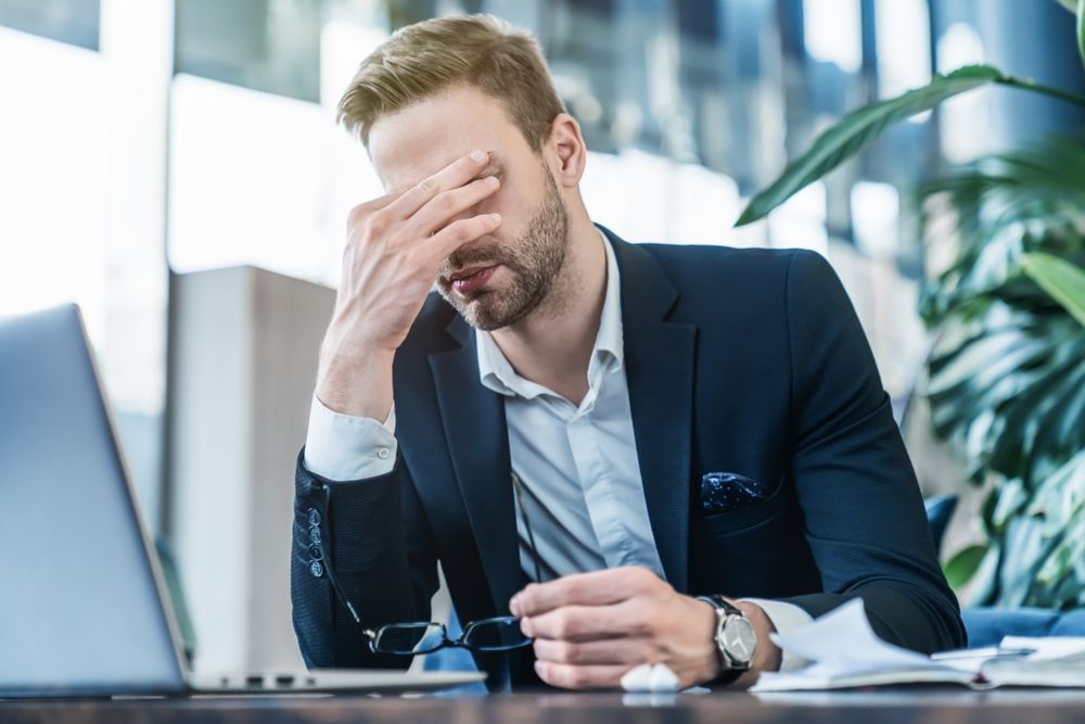 A man in a suit is sitting at a desk with his hand on his face.