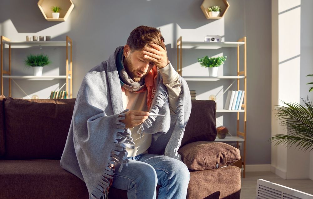 A man is sitting on a couch with a thermometer in his hand.