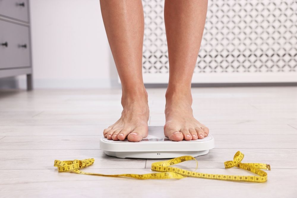 A woman is standing on a scale next to a measuring tape.