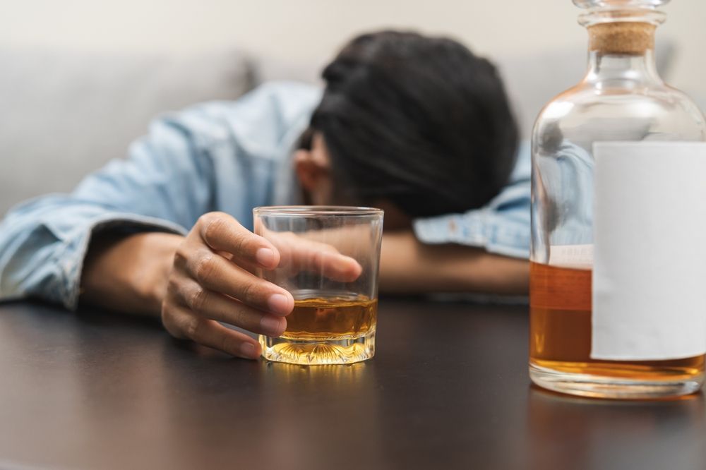 A man is holding a glass of whiskey next to a bottle of whiskey.