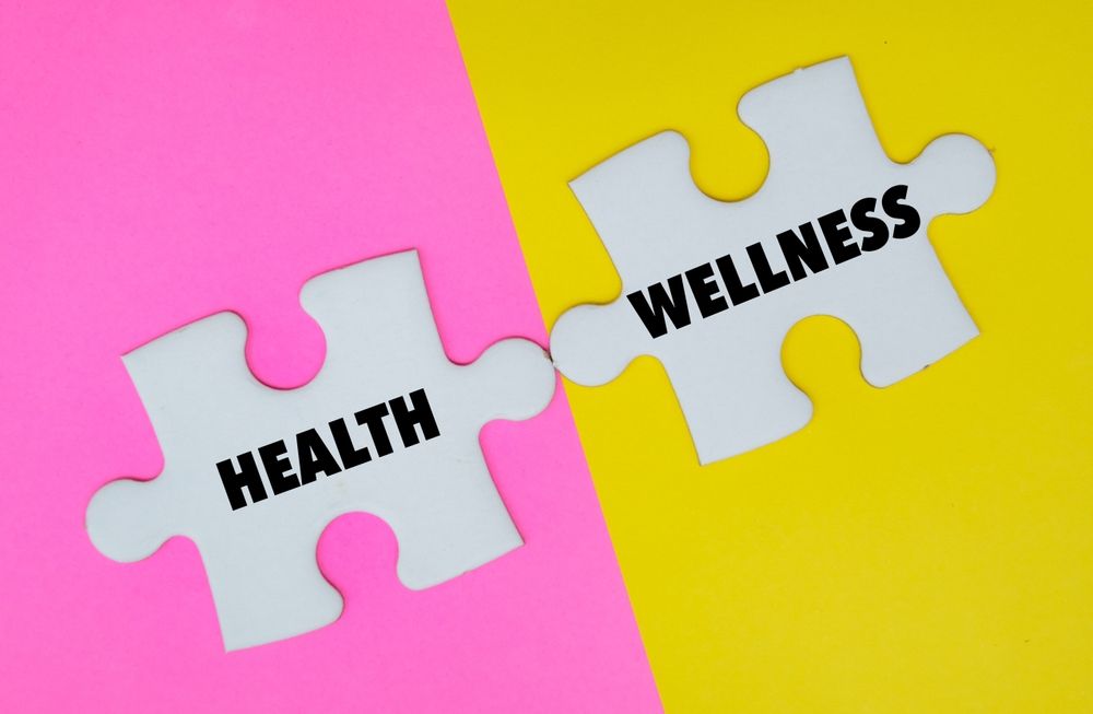 Two puzzle pieces with the words health and wellness written on them on a pink and yellow background.