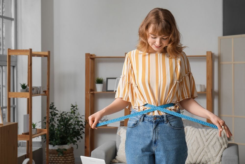 A woman is measuring her waist with a tape measure.