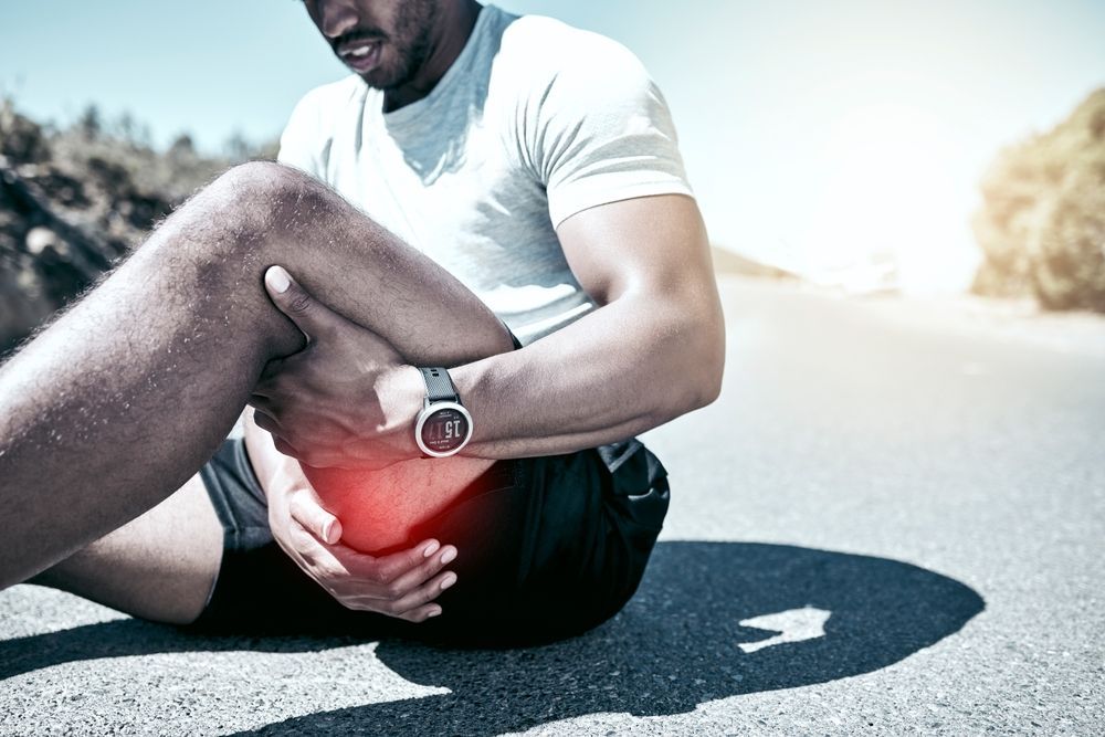 A man is sitting on the ground holding his knee in pain.