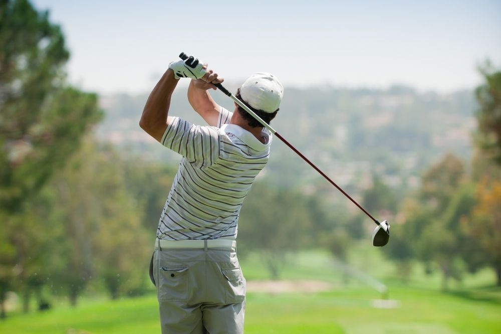 A man is swinging a golf club on a golf course.