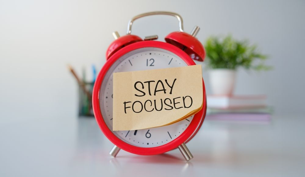 A red alarm clock with a sticky note on it that says `` stay focused ''.