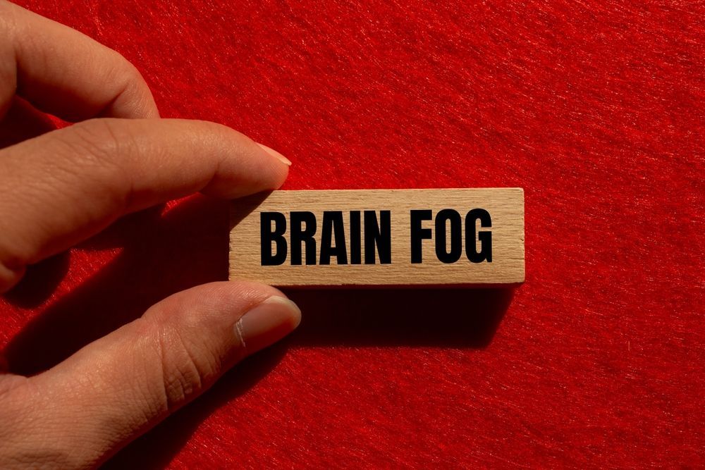 A person is holding a wooden block with the word brain fog written on it.