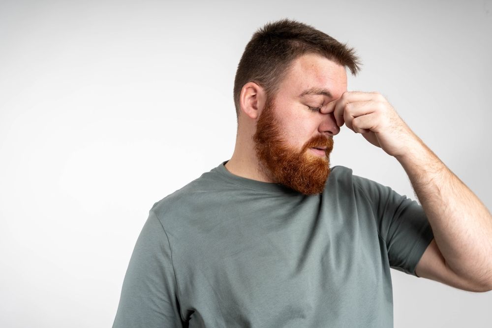 A man with a beard is covering his nose with his hand.