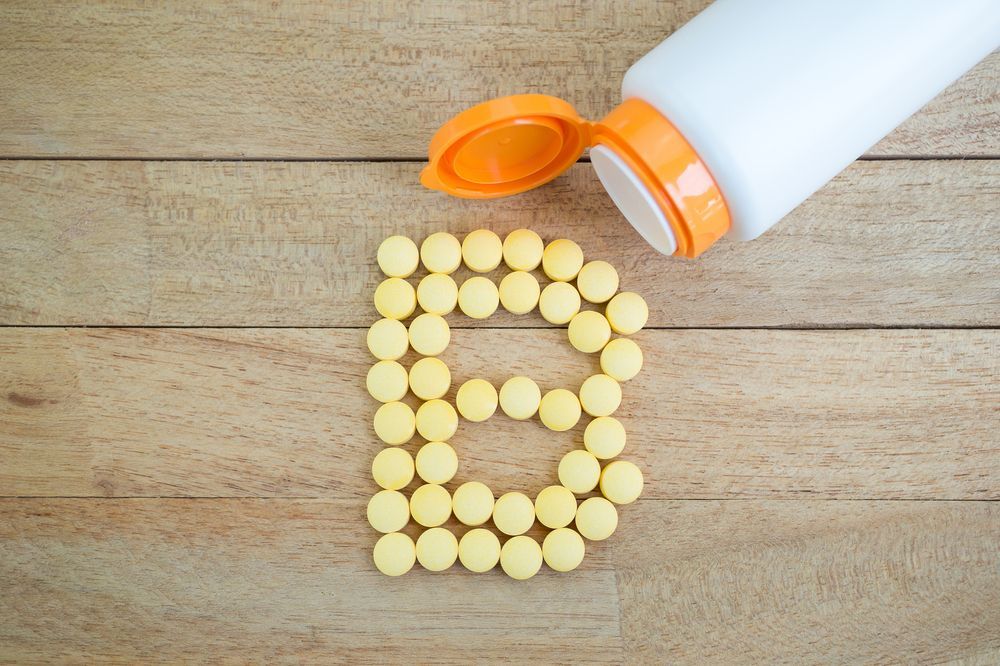 A bottle of vitamin b is being poured into a pile of pills on a wooden table.