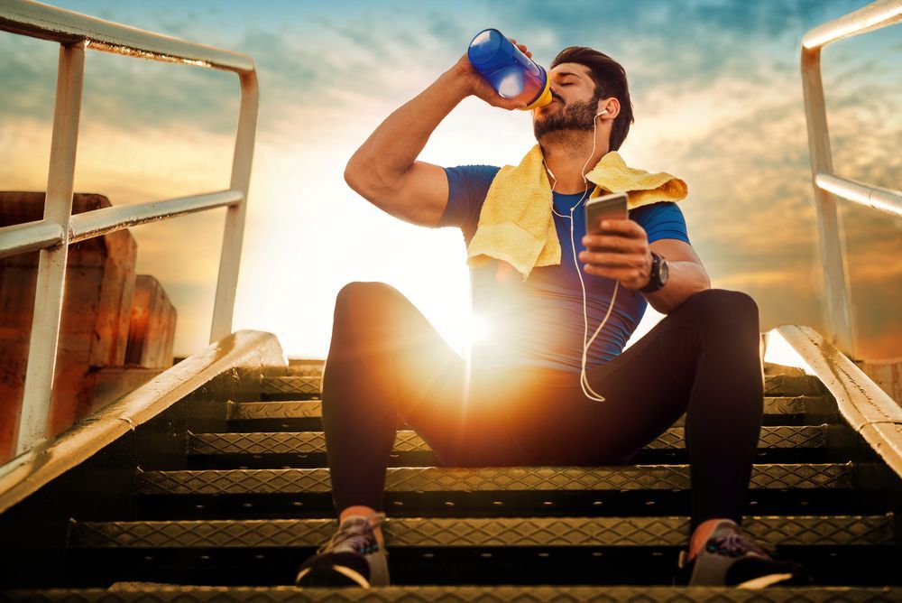 A man is sitting on a set of stairs drinking water from a bottle.