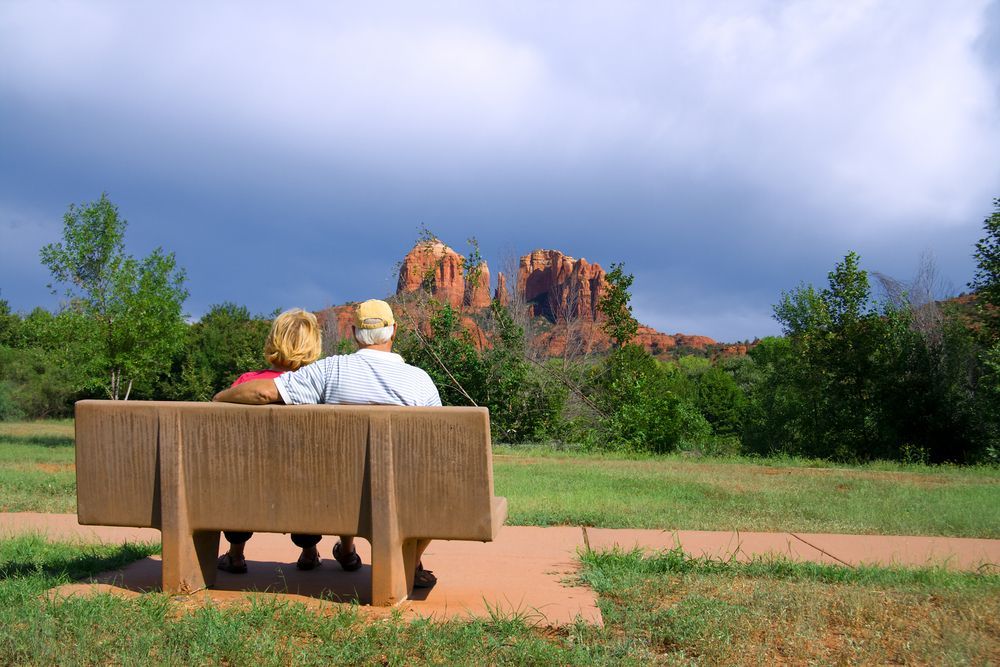 A man and woman are sitting on a park bench looking at a mountain.