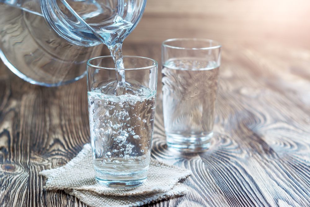 Water is being poured into two glasses on a wooden table.