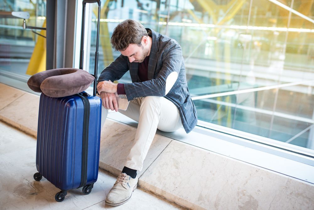 A man is sitting on the floor next to a suitcase at an airport.