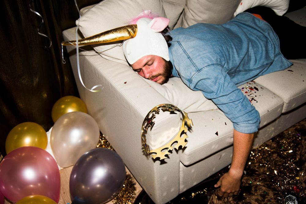 A man is laying on a couch with balloons and a tambourine.