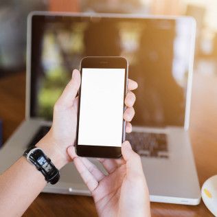 A person is holding a cell phone in front of a laptop.