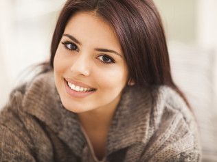 A woman is smiling for the camera while laying on a couch.