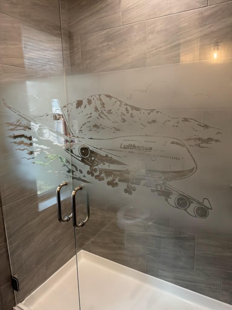 Frosted glass shower enclosure with etched fish design and chrome handles in a tiled bathroom