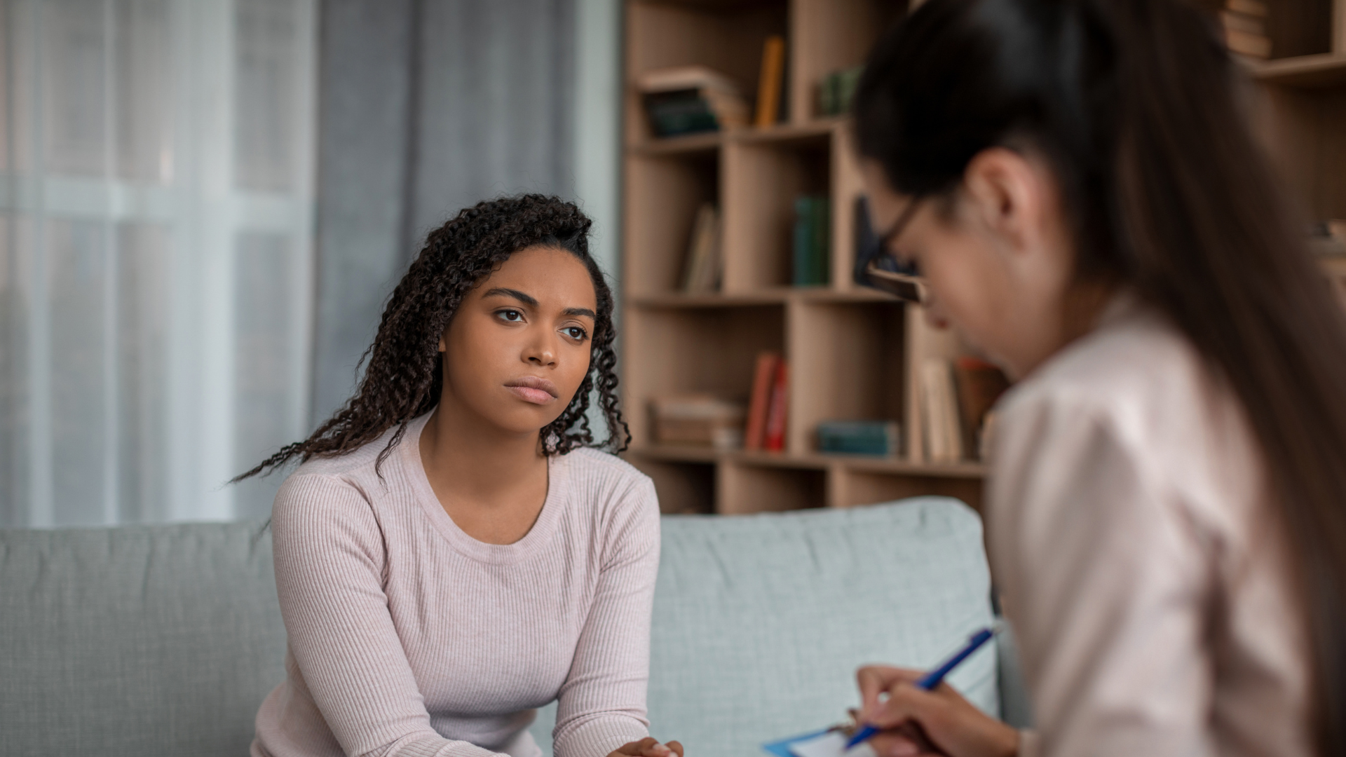 Therapist comforting a distressed client on a couch in a bright office
