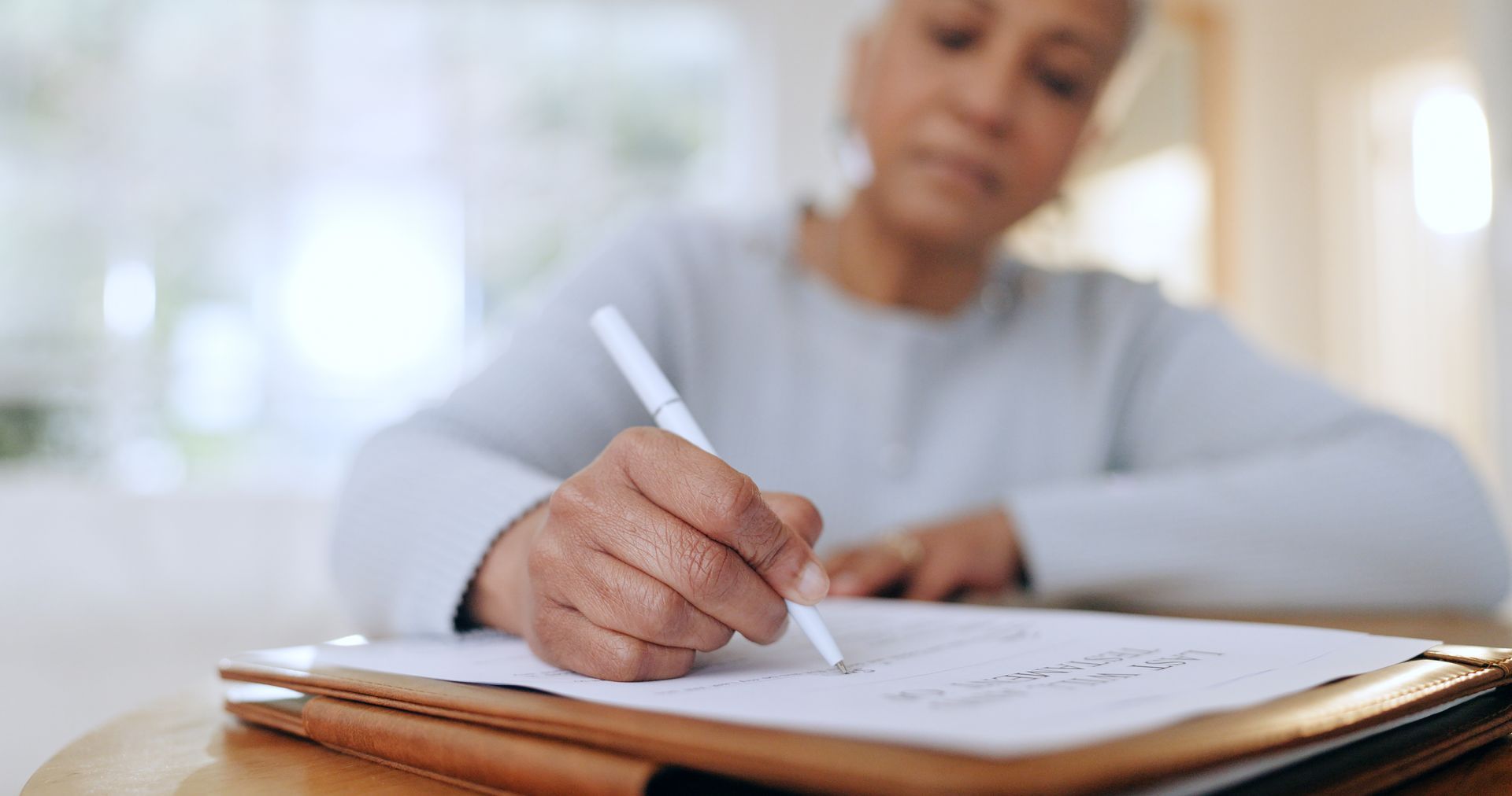 A senior woman writes her will on paper at home.
