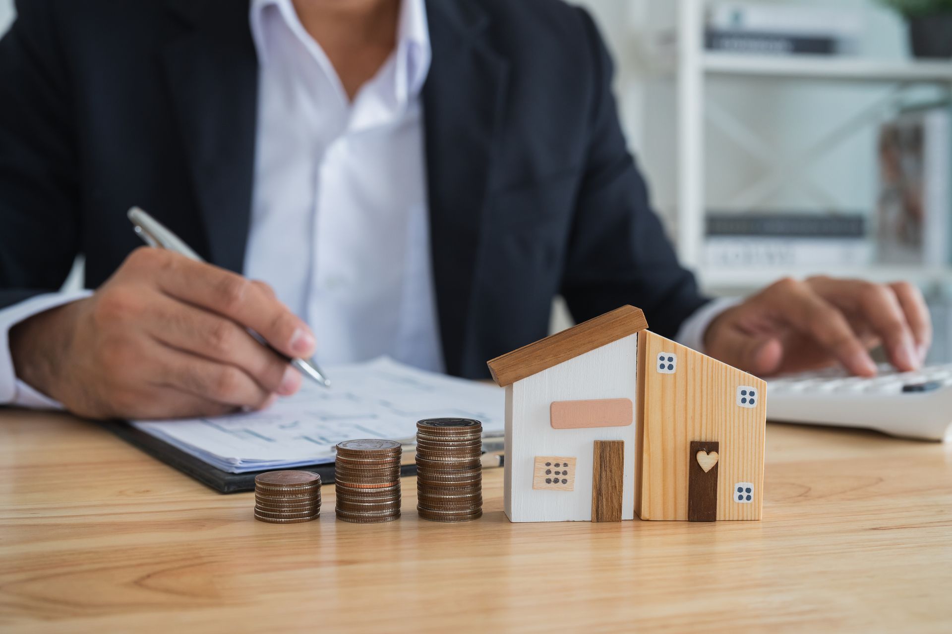 A wills lawyer signing estate documents besides coins and two different house models.
